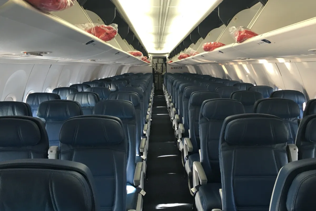 An empty narrow-body economy cabin photographed down the aisle before boarding, with rows of dark navy leather seats and bright cabin lighting