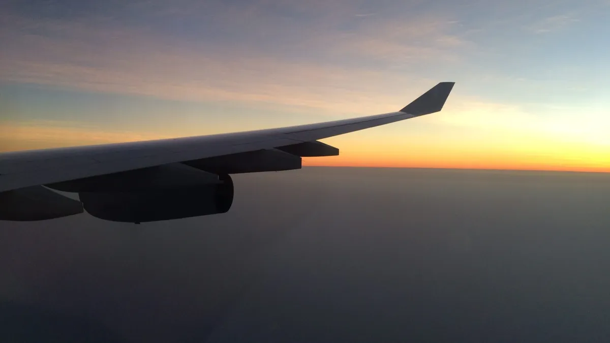 View from an aircraft window at sunset, the wing and engine silhouetted against a glowing horizon