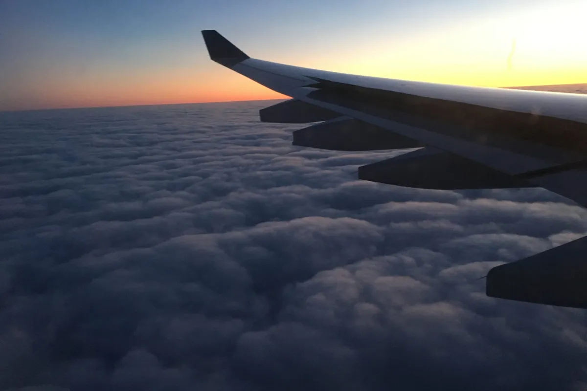 An aircraft wing above a blanket of cloud at sunset.
