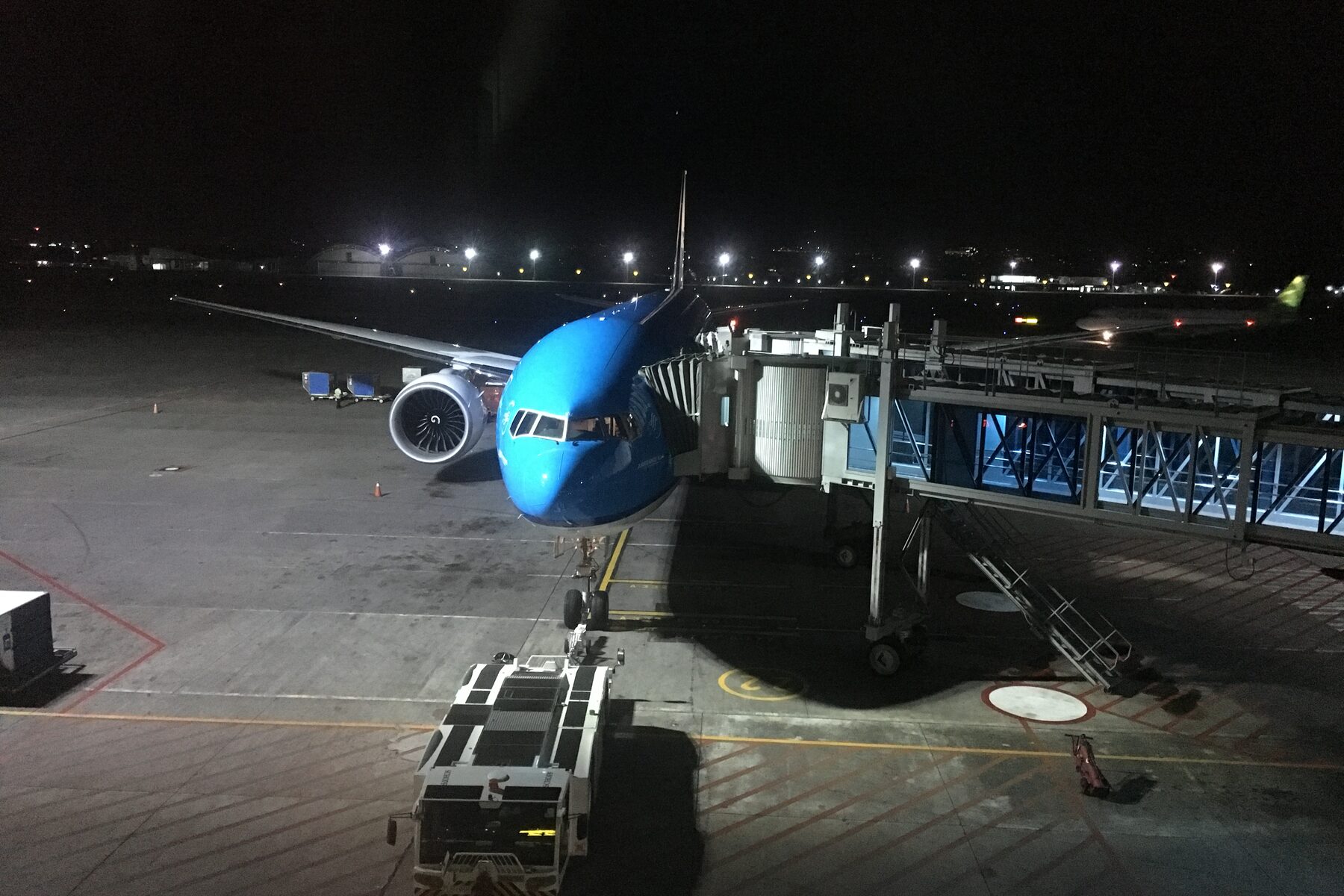 An aircraft parked at a gate at dusk with a jet bridge connected and ground equipment alongside.